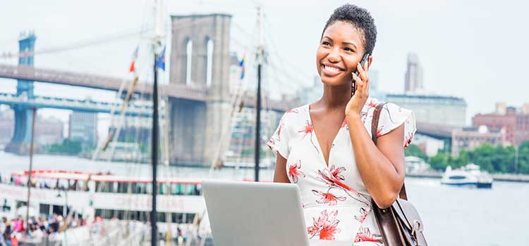 woman on phone and laptop checking news and current info in front of bridge